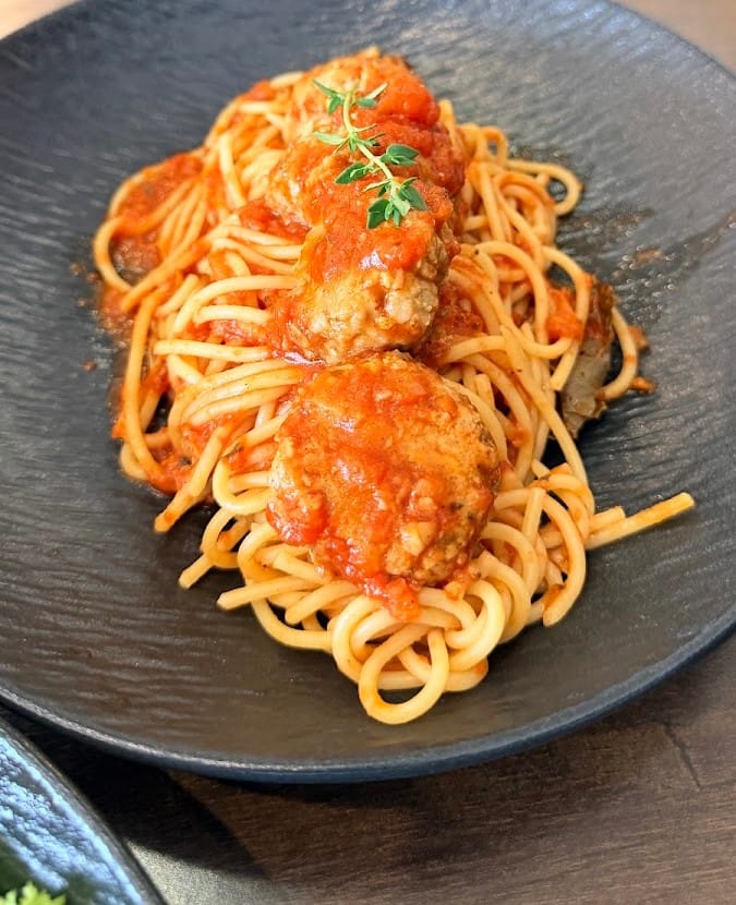 Spaghetti with meatballs in tomato sauce, topped with a sprig of herb
