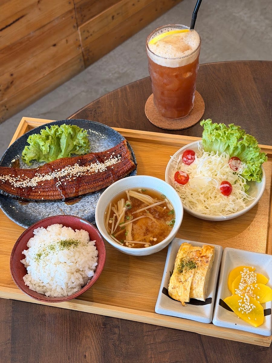 Grilled eel set with rice, miso soup, cabbage salad, rolled omelette and pickled radish, with an iced drink and a slice of lemon